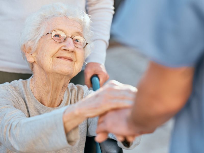 Holding hands, caregiver and senior woman in wheelchair for support outdoor in retirement home. Love, trust and healthcare nurse or medical wellness doctor for disability patient with kindness.