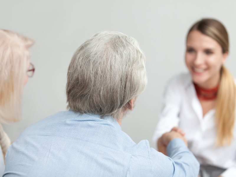 Rear view at senior couple handshaking medical worker visiting doctor, older family and financial advisor or lawyer shaking hands at meeting, happy grey-haired aged elderly clients making deal